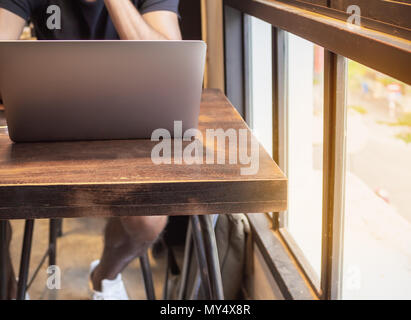The Man in Black Shirt Working with Silver Laptop Computer on Wooden Table Near The Window in Cafe Stock Photo