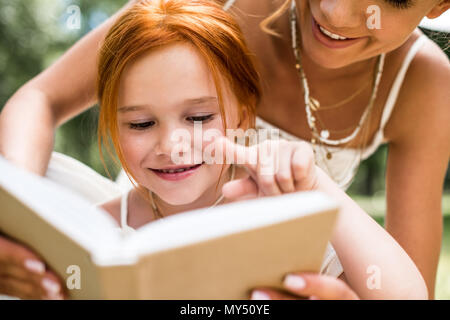 cropped shot of beautiful smiling mother and daughter reading book together in park Stock Photo