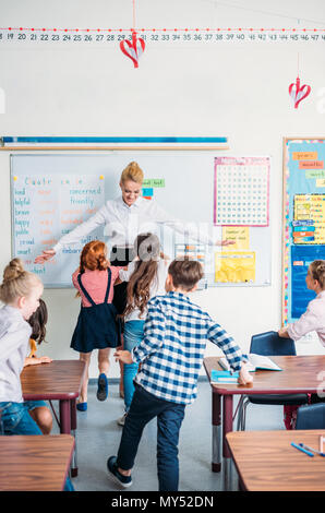 happy young teacher embracing with pupils in class Stock Photo