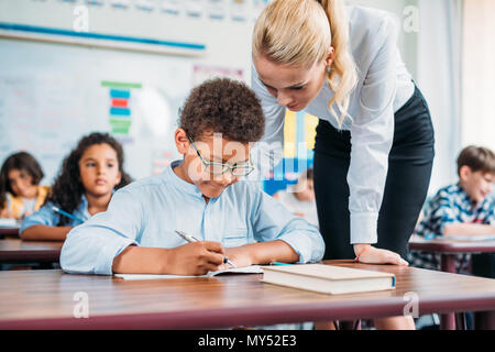 beautiful young teacher helping happy schoolboy with exercise Stock Photo