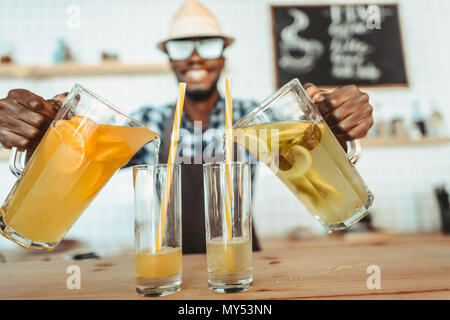 stylish african american bartender pouring lemonades into glasses on bar counter in cafe Stock Photo