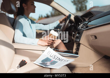Young woman driving a car with business newspaper lying in front seat
