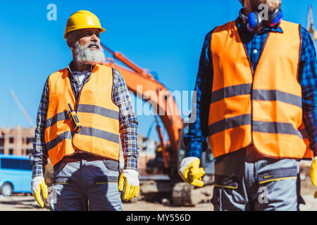 Two workers in reflective vests and hardhats standing at construction site Stock Photo
