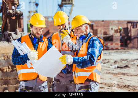 Three workers examining building plans at construction site Stock Photo