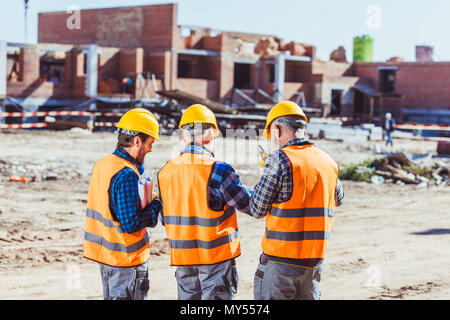 Three workers in hardhats and reflective vests standing at construction site Stock Photo