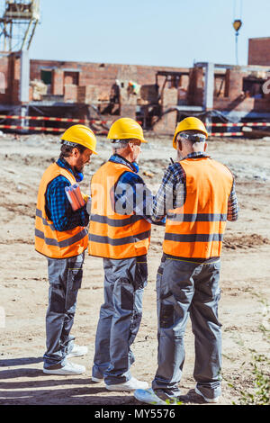 Three workers in hardhats and reflective vests standing at construction site Stock Photo