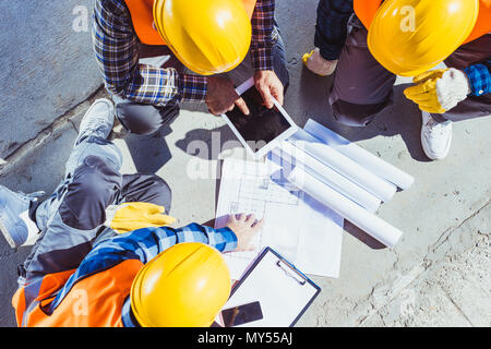 Three construction workers sitting on concrete and discussing building plans Stock Photo
