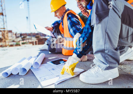 Cropped shot of construction workers in uniform sitting on concrete at construction site, examining building plans Stock Photo