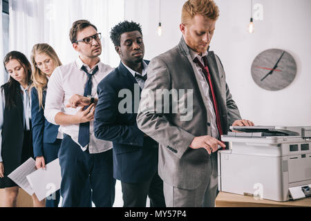 group of young managers standing in queue for copier at office Stock Photo