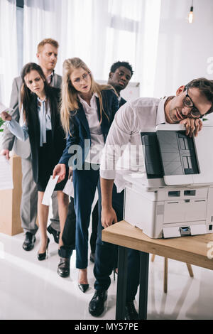 businessman sleeping on copier while his colleagues standing in queue behind him Stock Photo