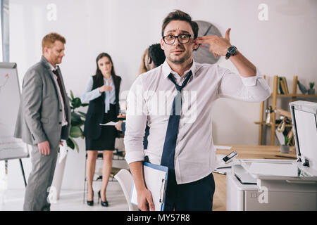 exhausted young manager making handgun gesture at office and looking at camera Stock Photo