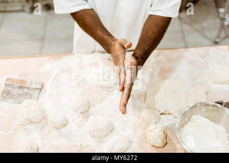cropped shot of african american baker preparing dough balls for pastry and covering hands in flour Stock Photo