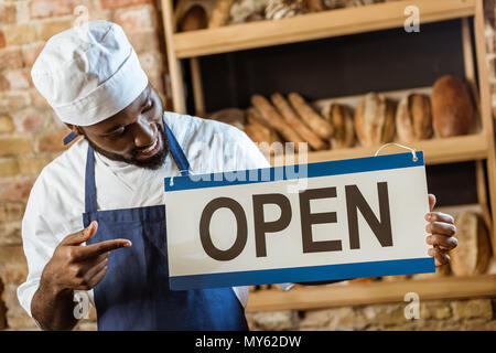 handsome african american baker pointing at open sign at pastry store Stock Photo