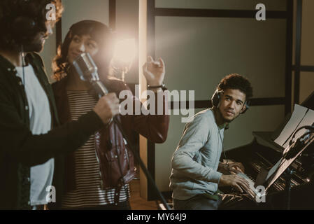 young couple performing song with microphone while man playing piano behind Stock Photo
