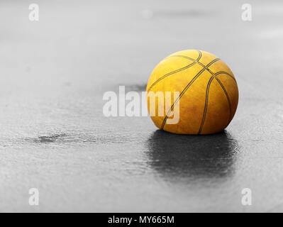 Black and white bw with single isolated colour yellow feature old used basketball. Flat deflated and let down. Stock Photo