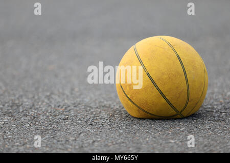 Right hand focus, close up of old tired deflated let down yellow basketball on a road surafce concept. needs air, worn out spent and discarded sport e Stock Photo