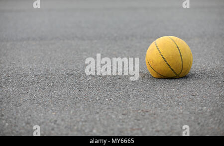 Right hand focus, wiede view of old tired deflated let down yellow basketball on a road surafce concept. needs air, worn out spent and discarded sport Stock Photo