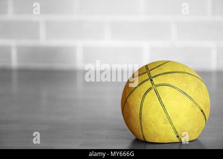 Close up black and white isolated colour color old tired let down deflated worn out spent basketball on a wooden court with blurred brick background.  Stock Photo