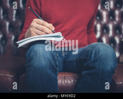 Close up on a man sitting on a sofa and writing in a notebook Stock Photo