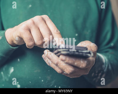 A young man with paint on his hands is using a smartphone Stock Photo