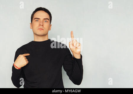 Attractive young man in white t-shirt pointing right with his finger on blue background. guy in a black t-shirt points one finger at himself with the  Stock Photo