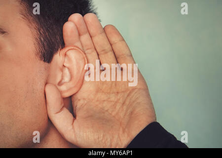 Listening male holds his hand near his ear. concept of deafness or eavesdropping. Hard of hearing. Stock Photo