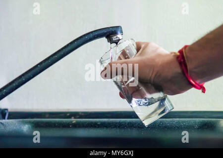 Closeup shot of a man pouring a glass of raw unfiltered drinking water from a kitchen tap. a man pours tap water into a glass transparent glass to dri Stock Photo