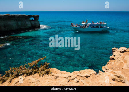 AYIA NAPA, CYPRUS, JUNE 15, 2017: Tourist boat approaching the sea caves of Ayia Napa from the sea. The littoral caves are one of the major tourist at Stock Photo