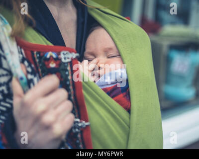 A young mother in the street with her baby in a carrier sling Stock Photo