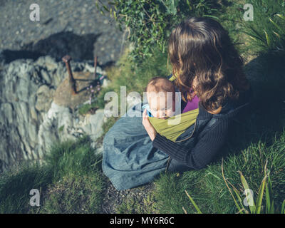 A young mother is sitting in nature with her baby in a sling Stock Photo