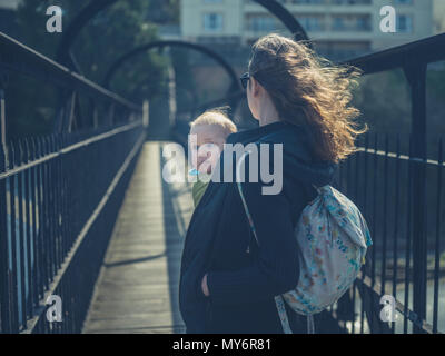A young mother is standing on a footbridge with her baby in a sling Stock Photo