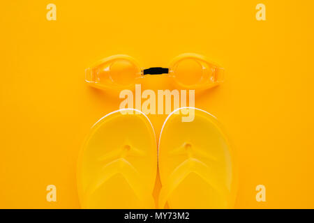 Swimming goggles and flip flops on yellow background, top view flat lay minimal composition Stock Photo