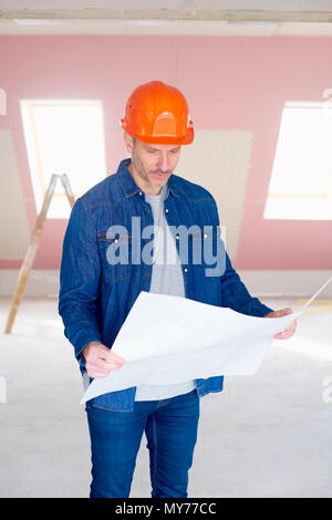 Middle aged construction worker holding plan in his hand while standing at construction site. Stock Photo