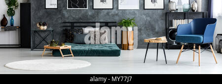 Wooden tray with green jug and tea cup standing next to mattress with pillows in dark grey bedroom interior with texture wall Stock Photo