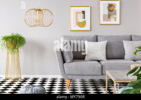 Real photo of a living room interior with gold posters on the walls, grey sofa with cushions and checkered floor Stock Photo