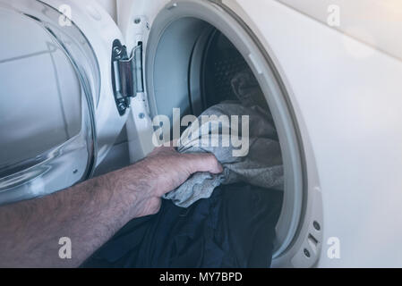 close-up of hand putting dirty laundry in drum of washing machine Stock Photo