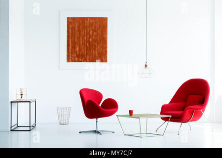 Red painting on white wall in modern apartment interior with armchairs at table. Real photo Stock Photo