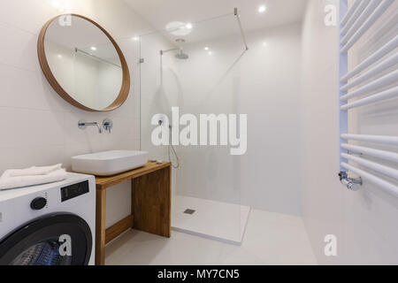 Mirror above washbasin in white bathroom interior with shower and washing machine. Real photo Stock Photo