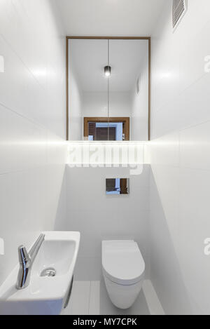 Mirror above toilet in white minimal bathroom interior with washbasin. Real photo Stock Photo