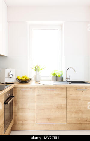 Flowers on wooden countertop in bright kitchen interior with window. Real photo Stock Photo