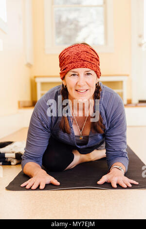 Portrait of senior woman practicing pigeon yoga pose (kapotasana) in yoga studio Stock Photo