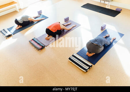 Three women practicing balasana (child's pose) in yoga studio Stock Photo