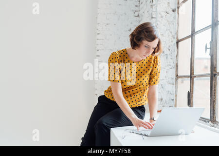 Businesswoman sitting on windowsill using laptop Stock Photo