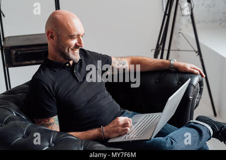 Man in armchair using laptop smiling Stock Photo