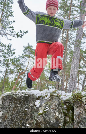 Young boy jumping from rock ledge, in rural landscape, low angle view Stock Photo