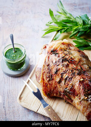 Roast leg of lamb on chopping board with jar of mint sauce, close-up Stock Photo