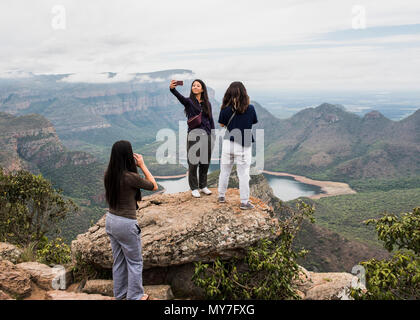 Three young female tourists looking out and taking selfie from The Three Rondavels, Mpumalanga, South Africa Stock Photo