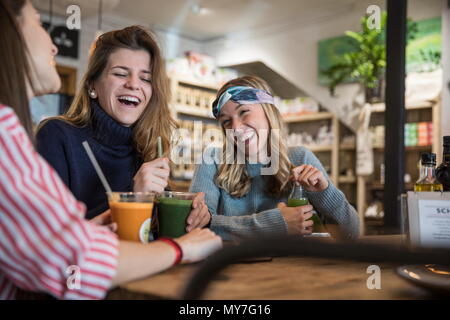 Three female friends, sitting in cafe, drinking smoothies, laughing Stock Photo