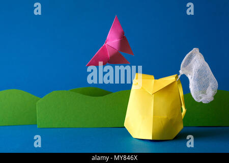 Paper backpack with butterfly net on grass field at blue background. Summer adventure. Camping and hiking or tourism concept. Origami. Paper cut. Stock Photo