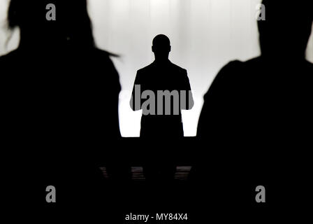 Silhouettes of a mystery man standing , watching and confronting two blurry persons in the dark Stock Photo